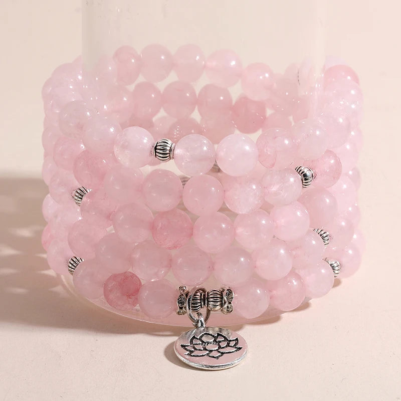 Bracelet mala en perles de quartz rose avec breloque Lotus argentée, enroulé plusieurs fois autour du poignet, posé sur un support rond