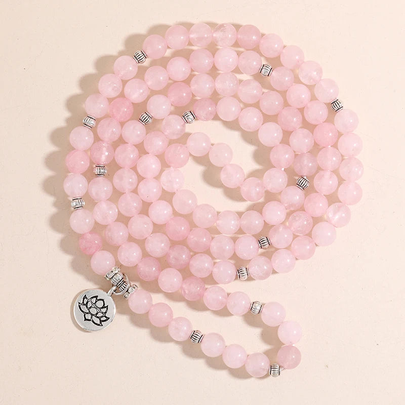 Bracelet mala en quartz rose déroulé en spirale sur fond rose clair, avec breloque Lotus argentée