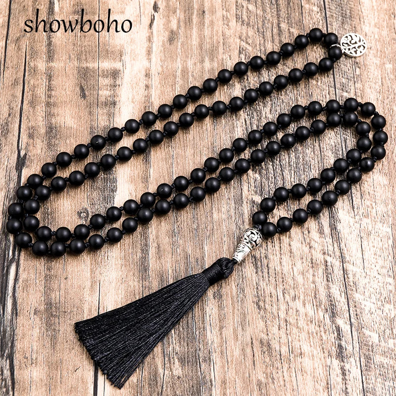 Collier mala 108 perles noires mates posé sur un fond en bois, pompon en soie noire et perle guide ouvragée argentée