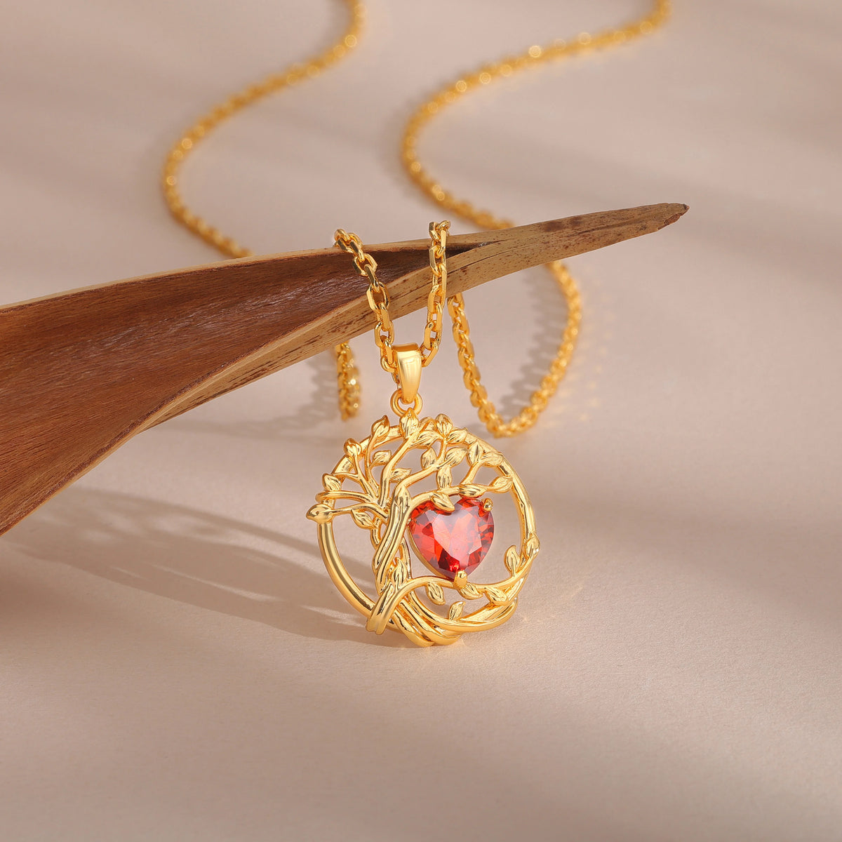 Collier Arbre de Vie en argent 925 finition dorée, pendentif suspendu devant un morceau de bois clair, pierre cœur rouge au centre