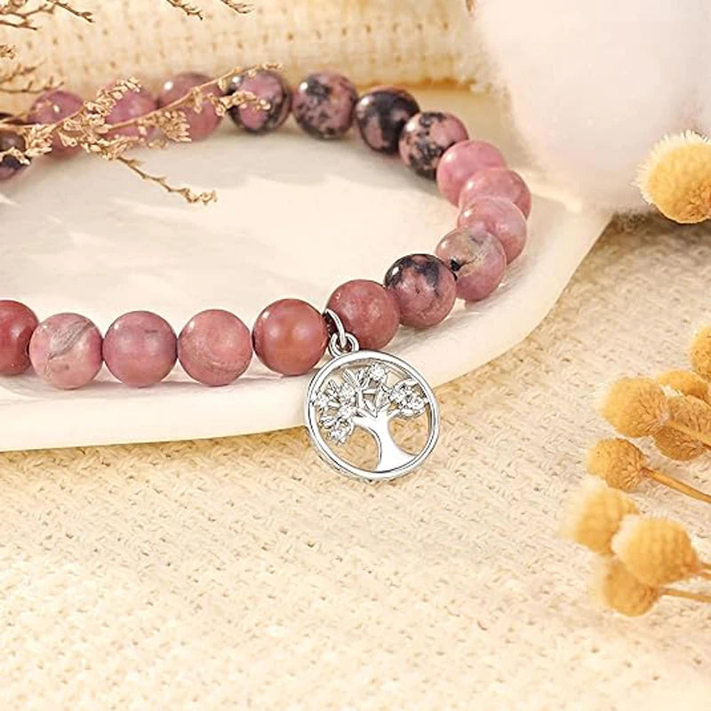 Gros plan sur la pampille arbre de vie argentée et les perles de pierre rose veinée de noir du bracelet
