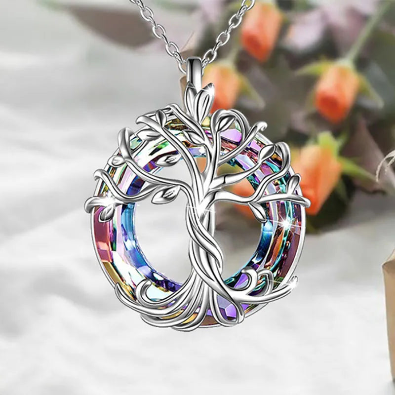 Collier Arbre de Vie Celtique en argent, cercle en cristal multicolore, suspendu devant un bouquet de fleurs orange en arrière-plan flou