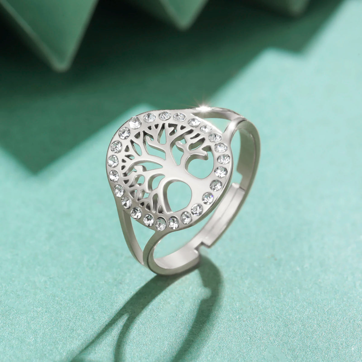 Gros plan sur la bague Arbre de Vie en acier argenté ornée de strass, posée sur un fond vert