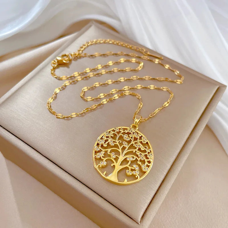 Collier Arbre de Vie avec pendentif rond serti de strass sur acier doré, chaîne posée sur une boîte satinée beige