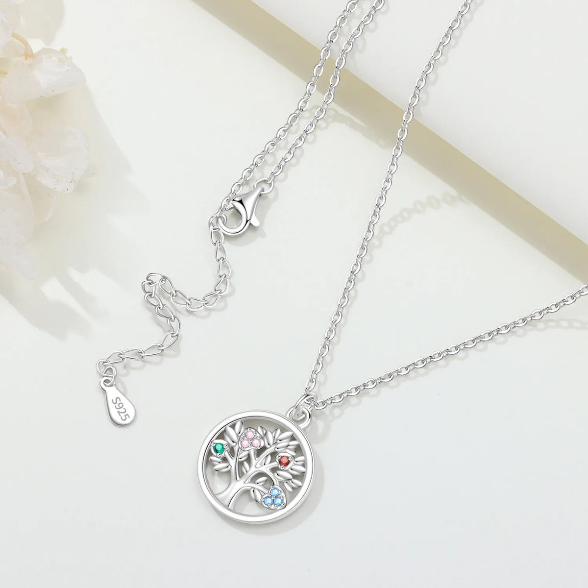 Pendentif Arbre de Vie en argent 925, chaîne et fermoir avec poinçon S925, posé sur fond clair fleuri