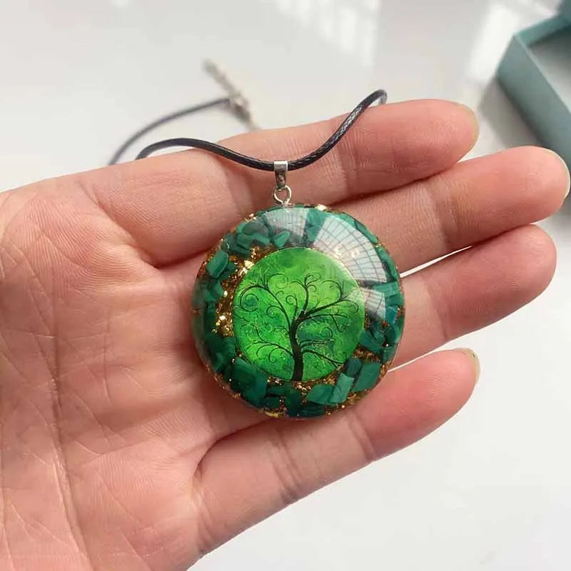 Pendentif Arbre de Vie en résine verte parsée d'éclats de malachite et de paillettes dorées, tenu dans une main pour l'échelle
