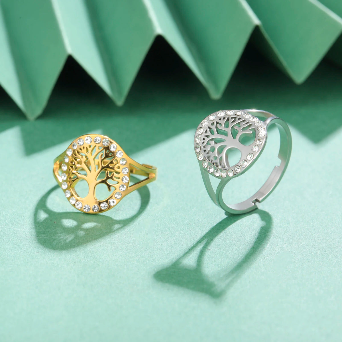 Bague Arbre de Vie en acier doré et sa version argentée, posées côte à côte sur un fond vert