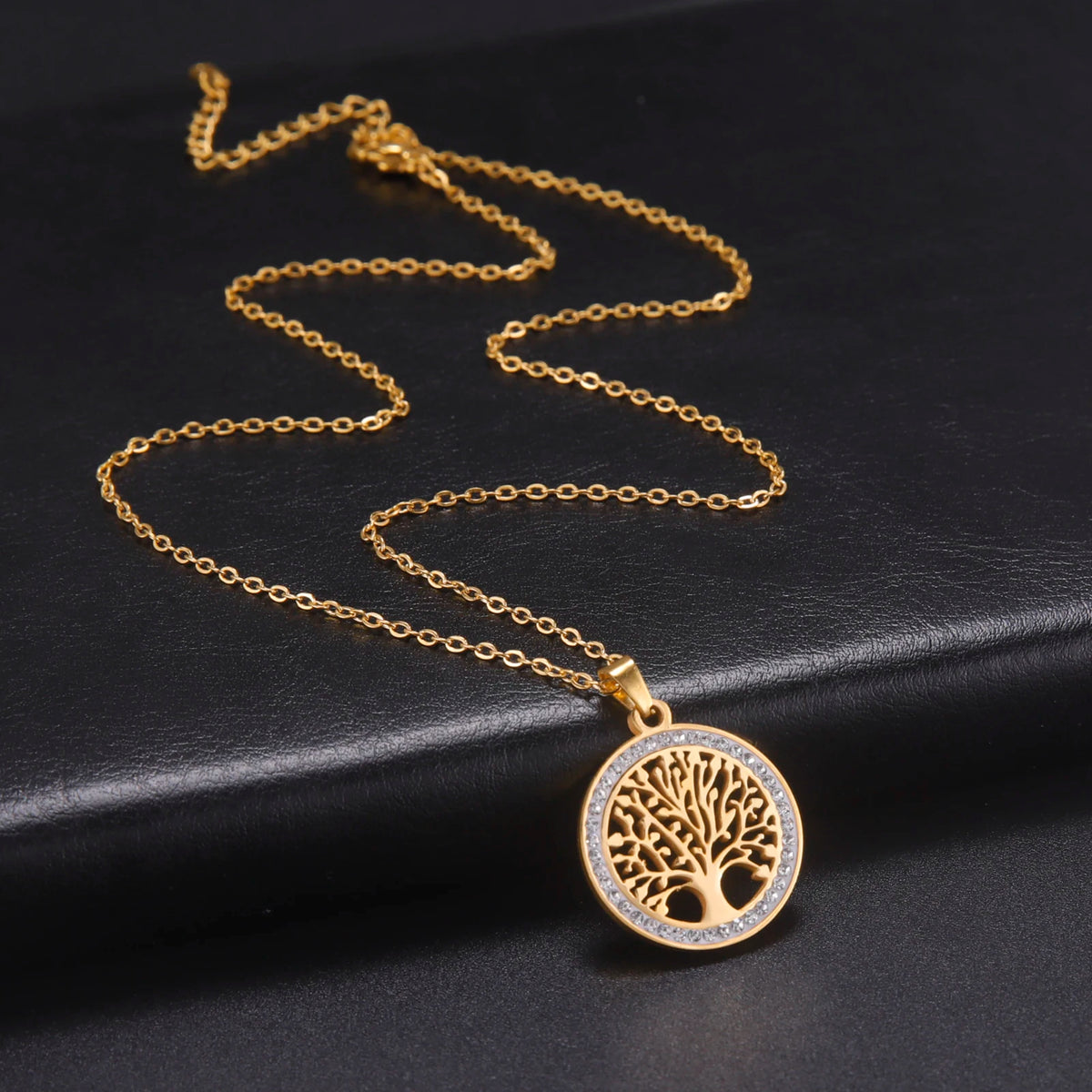 Pendentif Arbre de Vie doré serti de strass sur chaîne fine, posé sur fond noir