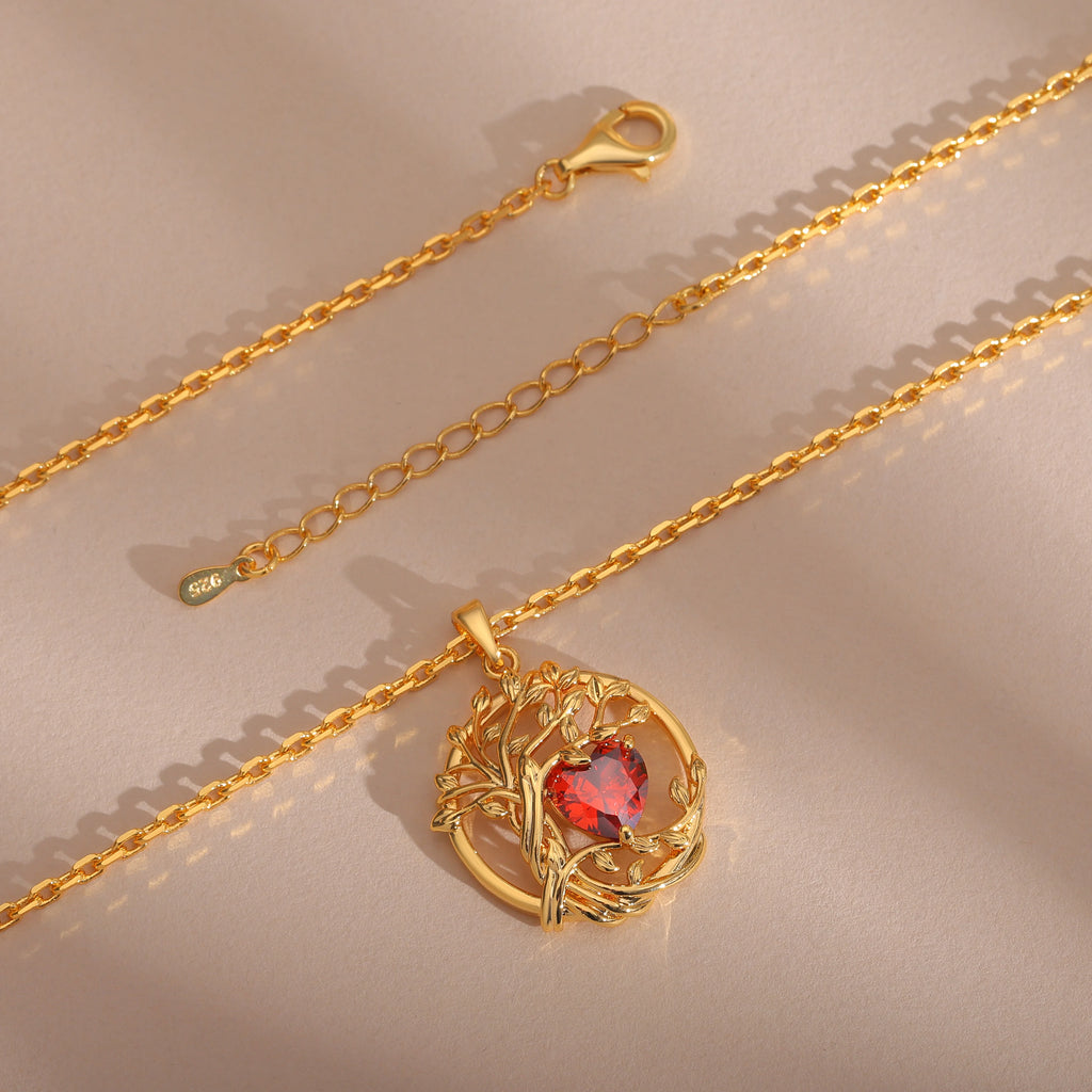 Collier Arbre de Vie en argent 925 finition dorée, pendentif rond avec arbre doré et pierre cœur rouge, chaîne posée sur fond beige