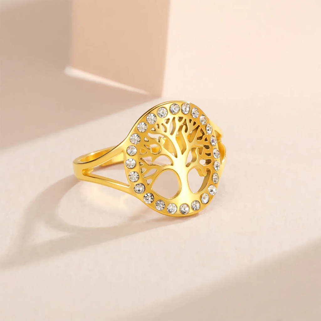 Bague Arbre de Vie en acier doré ornée de strass tout autour, posée sur un fond beige, vue de profil