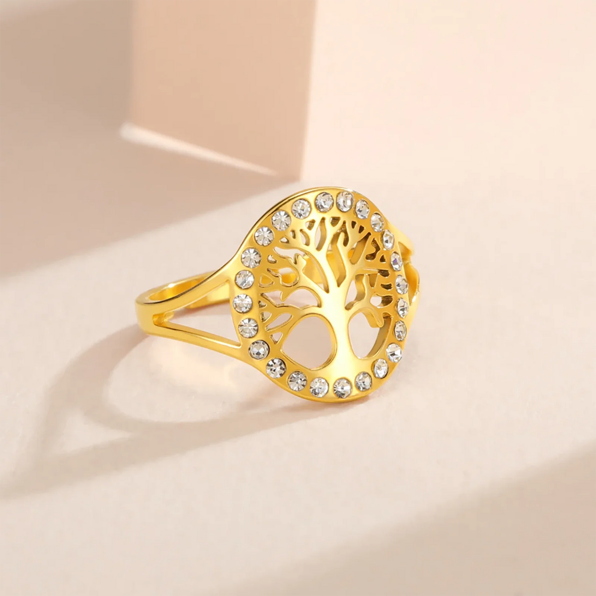 Bague Arbre de Vie en acier doré ornée de strass tout autour, posée sur un fond beige, vue de profil