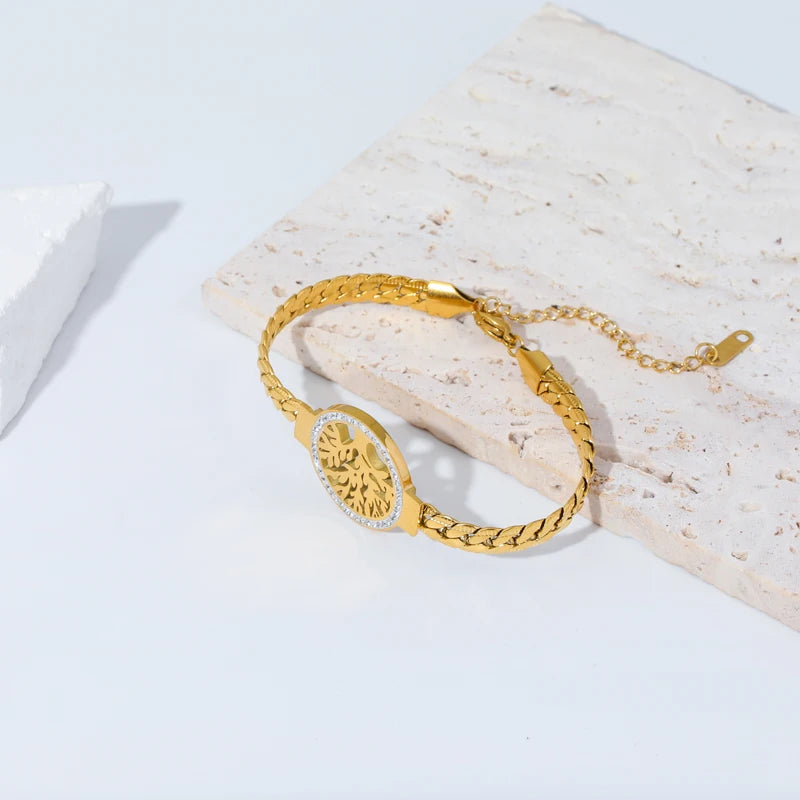 Bracelet Arbre de Vie en acier doré à maillons tressés, posé sur une plaque de pierre claire