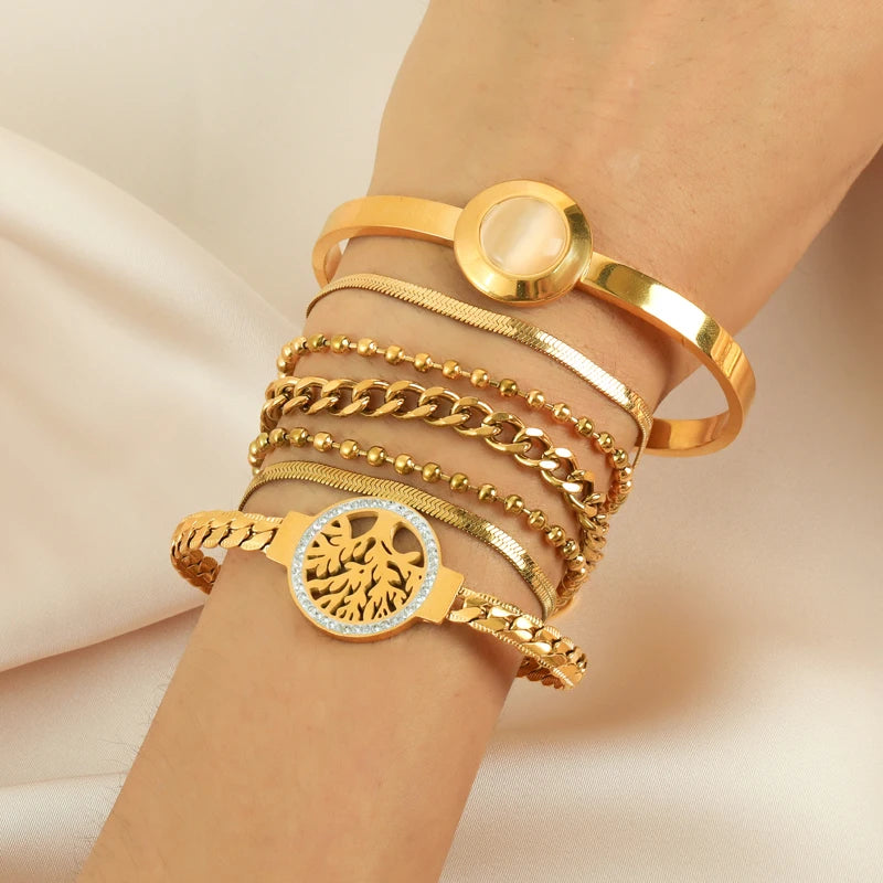 Bracelet Arbre de Vie en acier doré porté au poignet, empilé avec d'autres bracelets chaîne et maille dorés