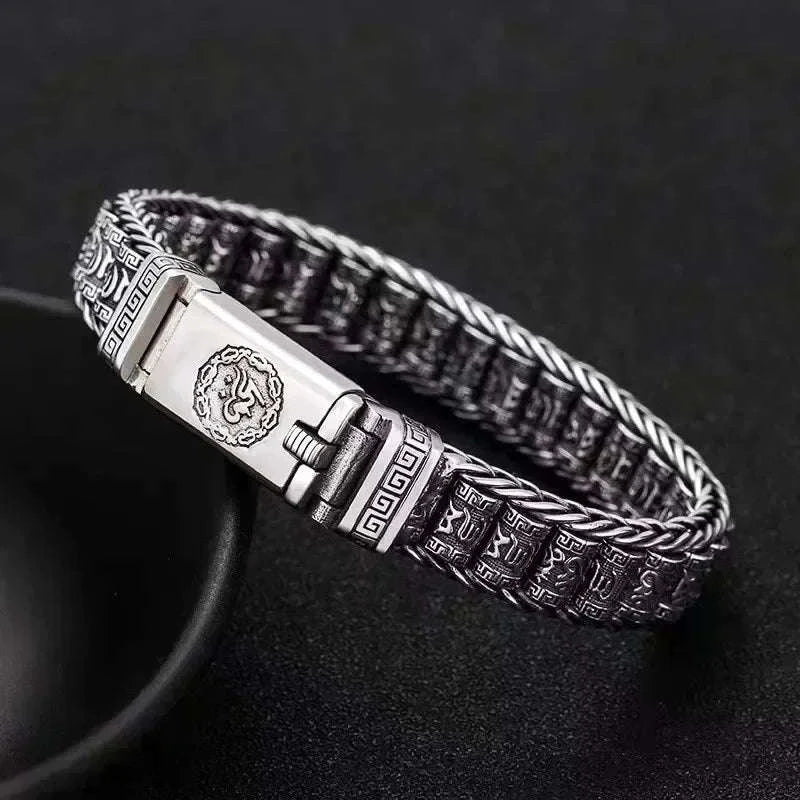 Bracelet jonc en argent à maillons tressés et cylindres gravés de mantras, posé en angle